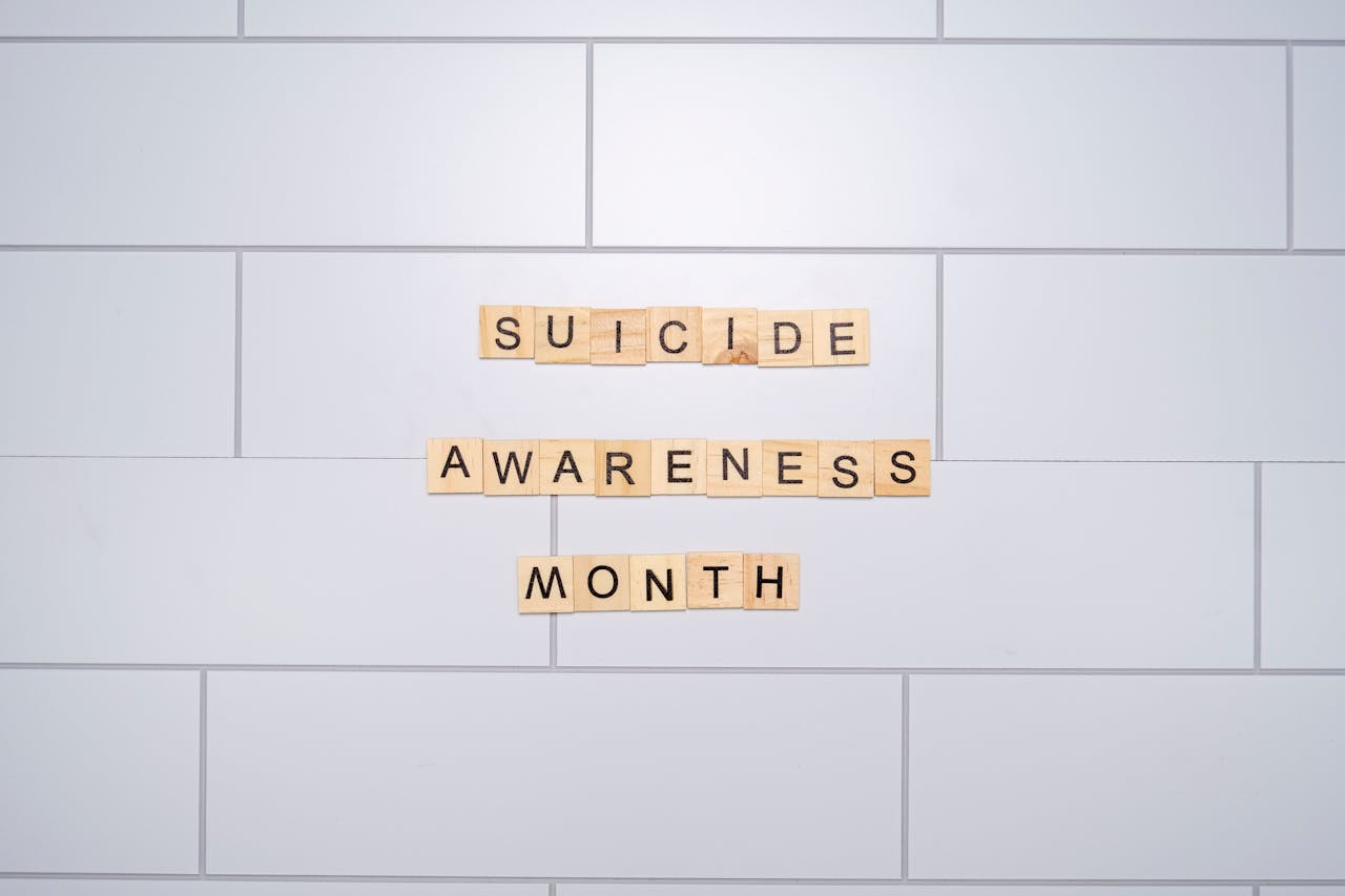 Suicide Awareness Month spelled with Scrabble tiles on a light background symbolizes mental health awareness.