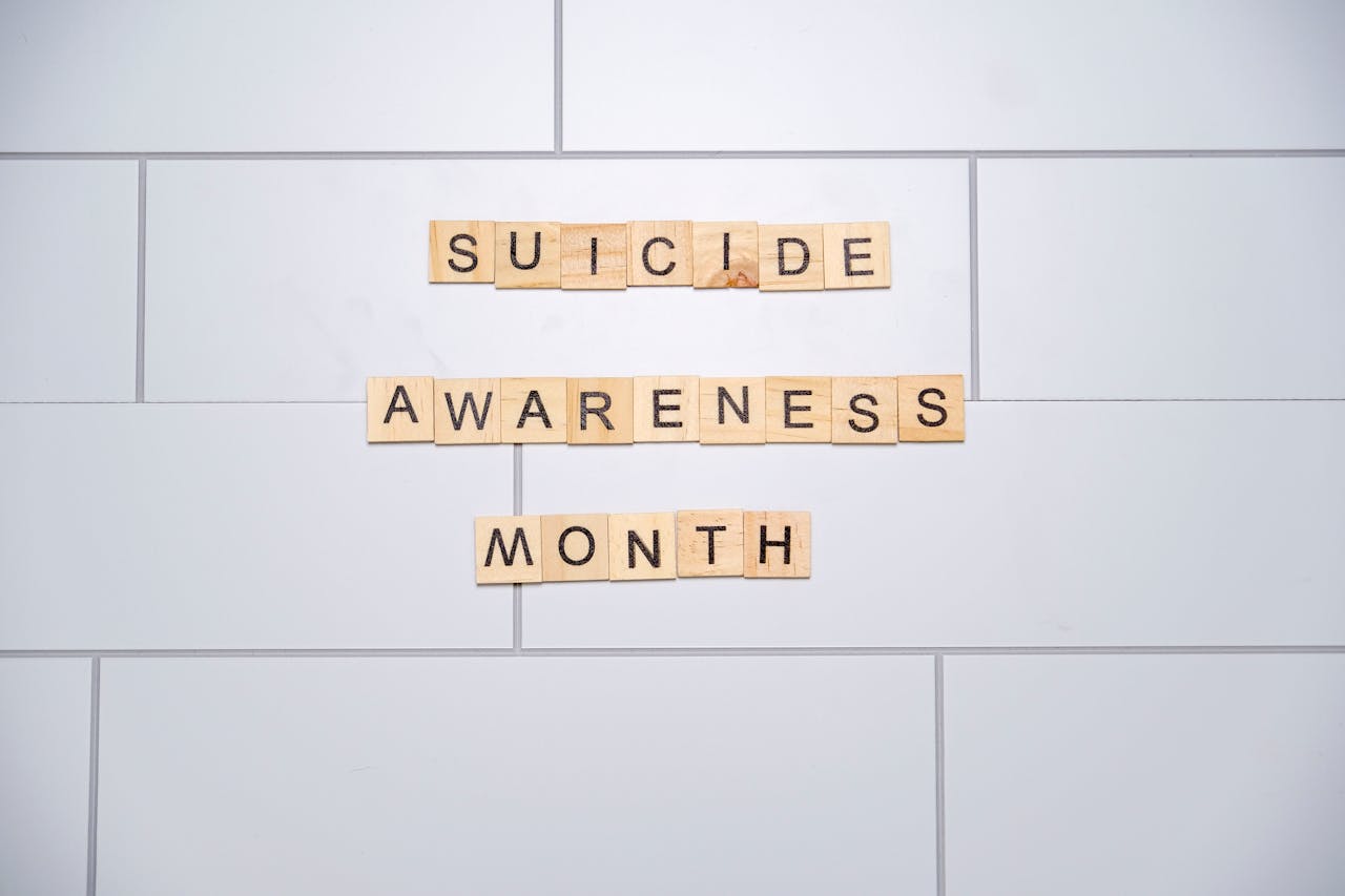 Wooden tiles spelling 'Suicide Awareness Month' on a white tiled background.