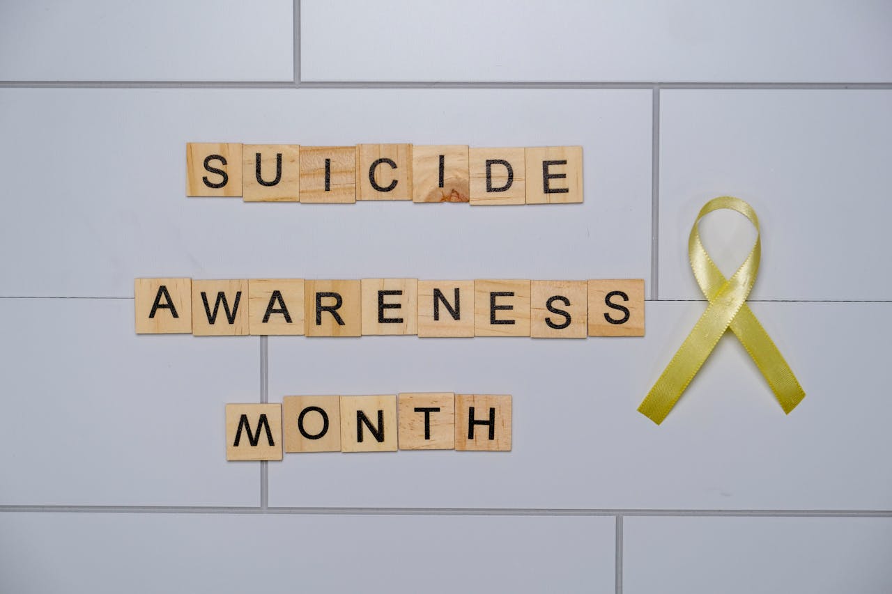 Wooden blocks spelling 'Suicide Awareness Month' with a yellow ribbon.