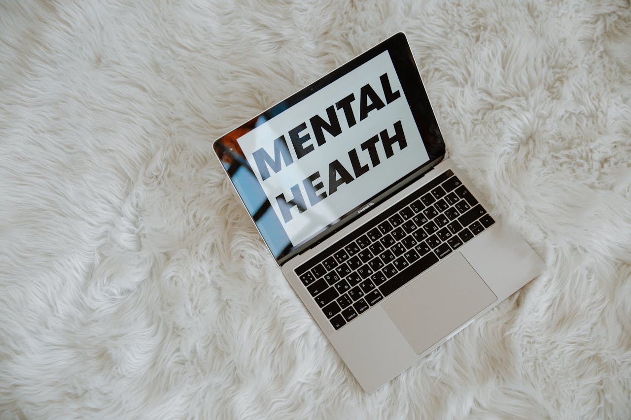 A laptop on a fluffy surface highlights the phrase 'Mental Health', emphasizing awareness.